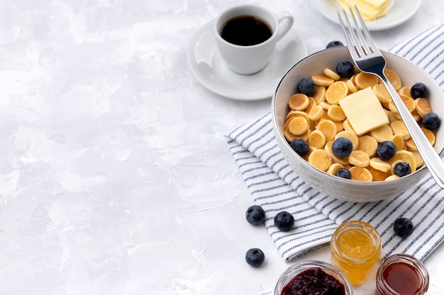 Tiny mini pancake cereal. Home made breakfast with blueberries, jam and coffee on gray background