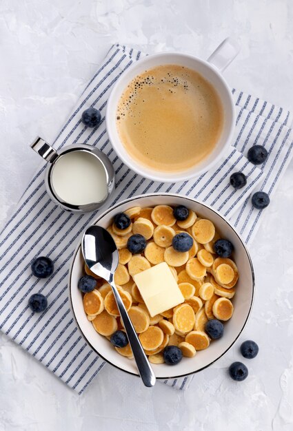 Tiny mini pancake cereal. Home made breakfast with blueberries, jam and juice on gray background