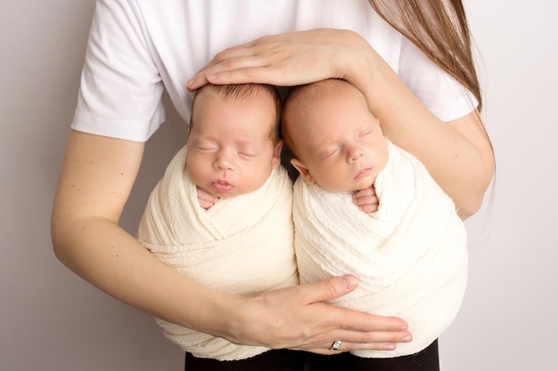 Tiny newborn twins boys in white cocoons in their mother39s arms The mother holds the twin children in her arms Studio professional photography of newborn twins