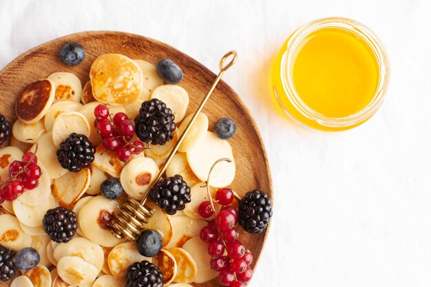 Tiny pancakes with berries in close-up on a white tablecloth