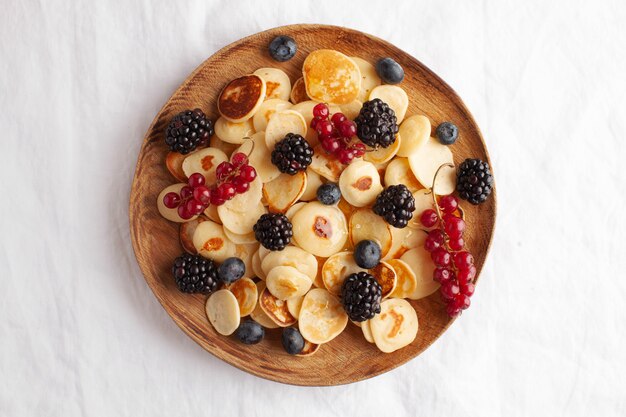 Tiny pancakes with berries in close-up on a white tablecloth