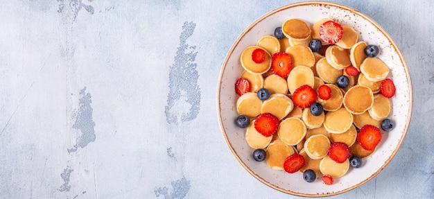 Tiny pancakes with strawberries and blueberries for breakfast. Top view.