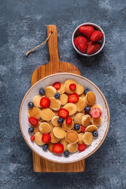 Tiny pancakes with strawberries and blueberries for breakfast. Top view.