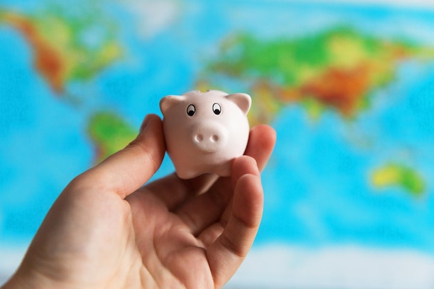 A tiny piggy bank is held in the hand A colourful map of the world in the background