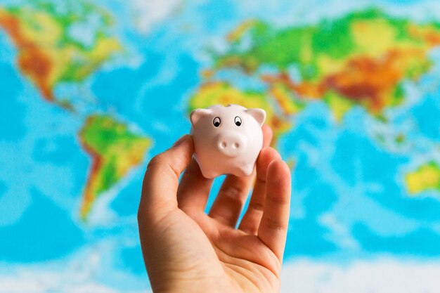 A tiny piggy bank is held in the hand A colourful map of the world