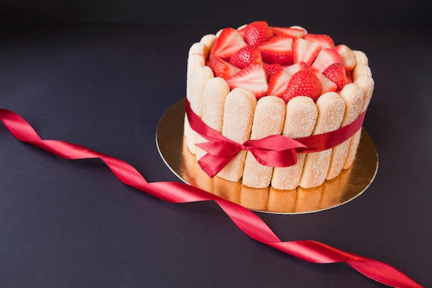 Tiramisu cake with strawberries ladyfingers mascarpone and red bowtape on black charlotte cake