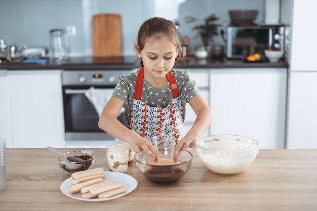 Tiramisu making process in the kitchen little girl making Italian desert with cocoa and espressodipped ladyfingers with mascarpone cream step by step 8