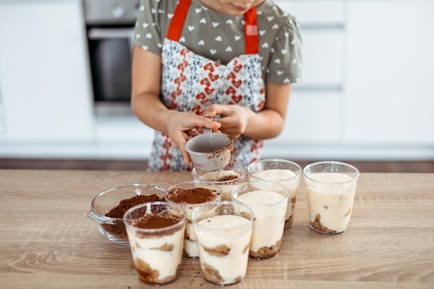 Tiramisu making process in the kitchen little girl making Italian desert with cocoa and espressodipped ladyfingers with mascarpone cream step by step 9