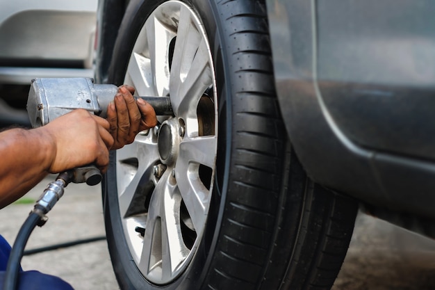 Tire Replacement concept. Mechanic Using Electric Screwdriver Wrench for Wheel Nuts in Garage. Car Maintenance and services