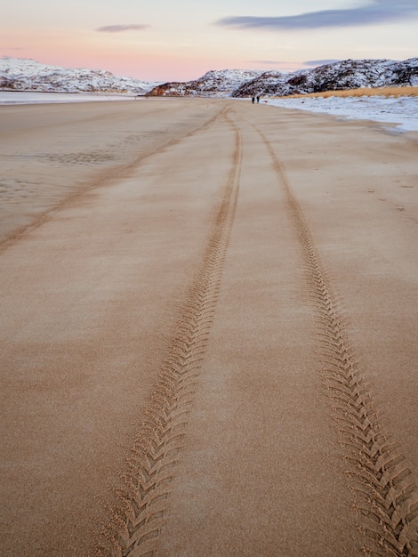 Tire tread mark on the sea sand extending into the distance.