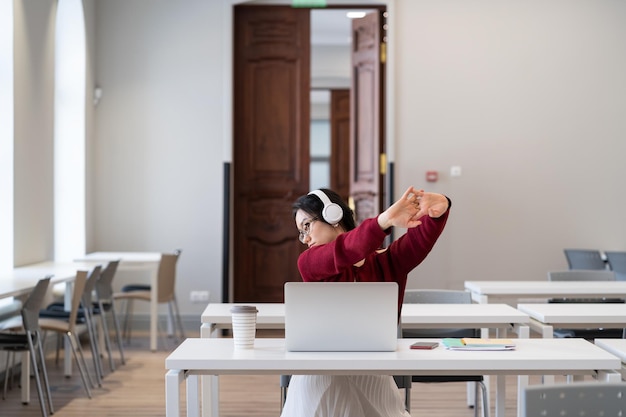 Tired asian female student sitting in library taking break during online learning on laptop