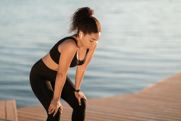 Tired black lady jogging by seaside having break