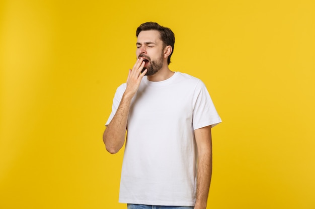 Tired or bored Caucasian hipster young man covering mouth while yawning, feeling exhausted after hard day at work