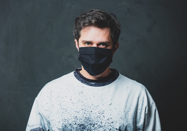 Photo tired brunet man in in black facemask on dark wall