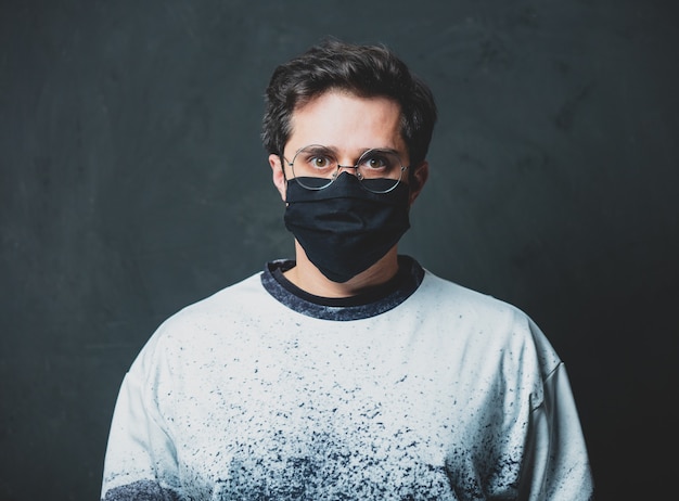 Photo tired brunet man in in black facemask on dark wall