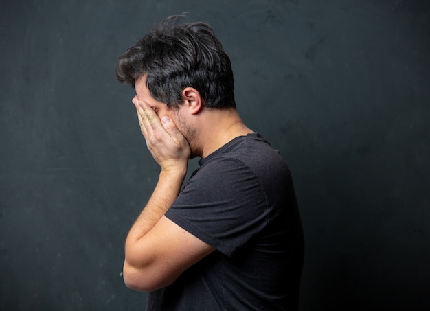 Photo tired brunet man in black t-shirt on dark wall