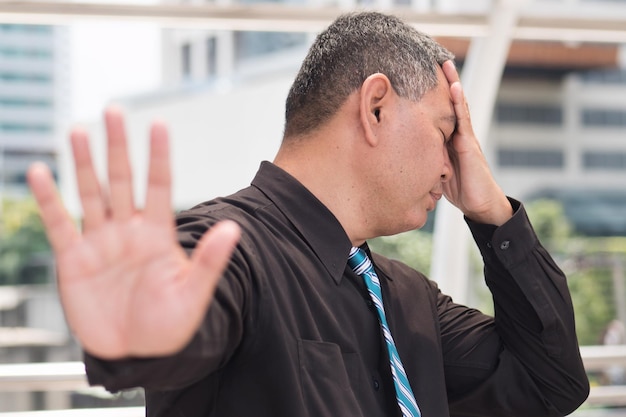 Tired business man saying no portrait of exhausted tired asian businessman showing stop halt hand gesture headache 50s old southeast asian man model