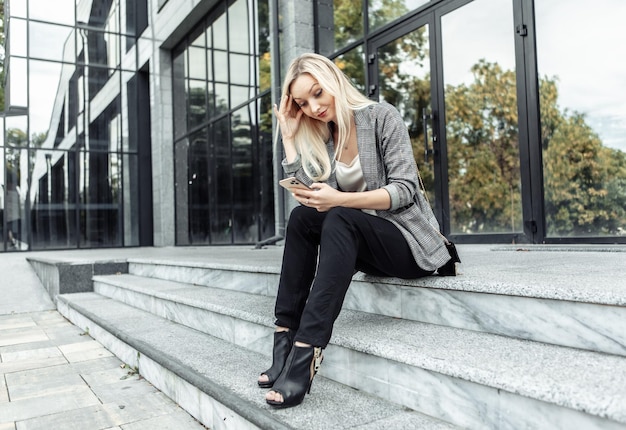 Tired Business woman sitting on the stairs and talking on phone on the background of business office