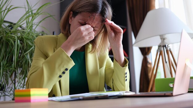 Tired business woman takes off glasses feeling tired eyes from working at computer overwork