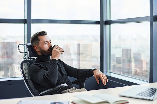 Tired businessman drinks coffee sitting at his desk