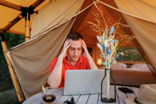 Tired businessman freelance using laptop on cozy glamping tent in a summer day Luxury camping tent for outdoor holiday and vacation Lifestyle concept