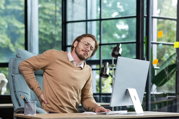 Tired businessman at workplace has severe back and lower back pain young man working sitting at