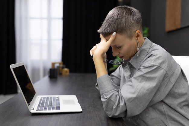 Tired businesswoman sitting in front of a laptop screen holding her head against the backdrop of a