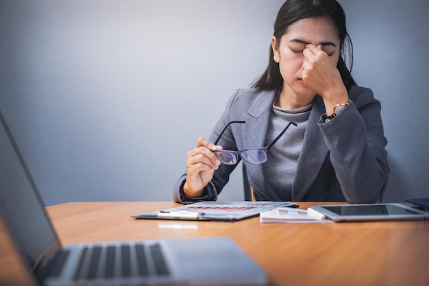 Tired businesswoman taking off glasses with eye pain during working in office overwork.