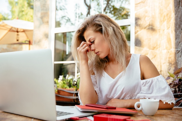 Tired businesswoman working with laptop, while sitting at the cafe, outdoors