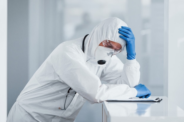 Tired doctor scientist in lab coat, defensive eyewear and mask takes break