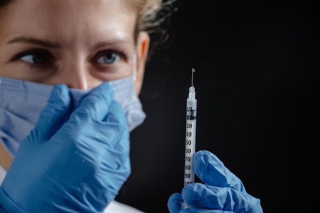 A tired doctor with a syringe on a black background the doctor adjusts the mask on his nose