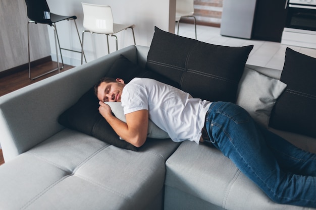 Tired exhausted guy lying on couch in horizontal position and daydreaming. Enjoy it alone. Sleep tightly. Calm peaceful moment.