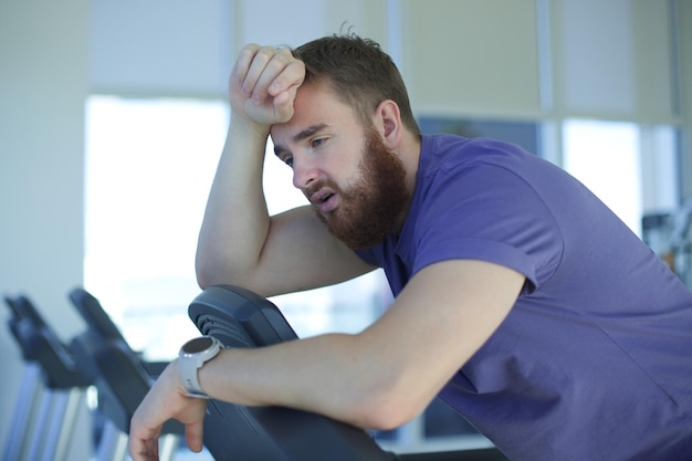 Tired exhausted young man feeling bad unhealthy unwell during run on treadmill in the gym