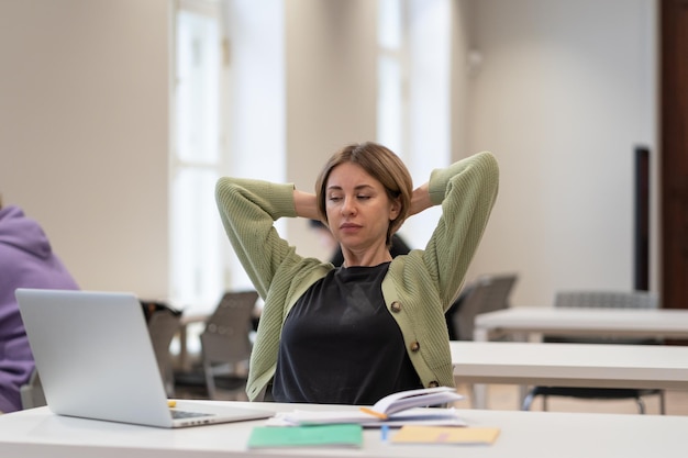 Tired female mature student taking break stretching arms while studying online in university library