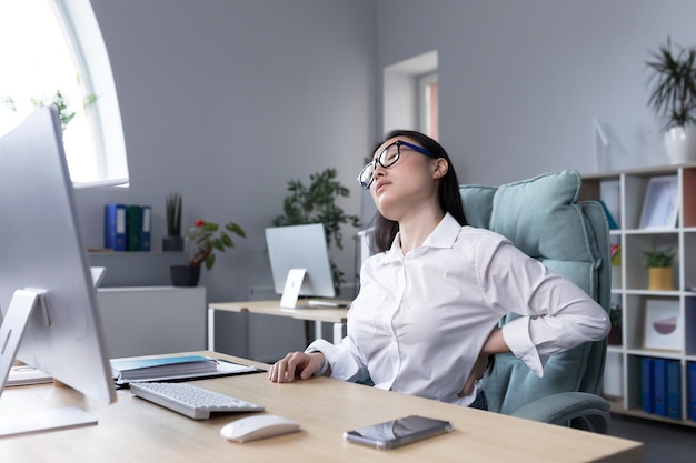 Tired female office worker massaging her back asian business woman has severe back and lower back