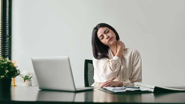 Tired female office worker massaging her neck to relieve pain after sedentary computer or work in incorrect posture