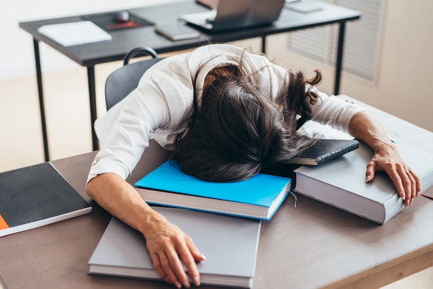 Tired female teacher sleeping on desk face and hands on books.