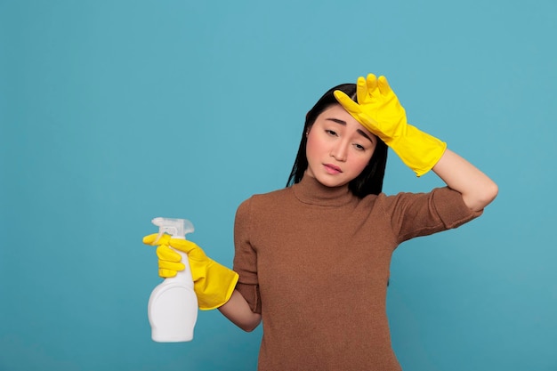 Tired frustrated and unhappy asian housewife from all the cleaning wearing yellow rubber gloves. Exhausted stressed overworked maid from housework and chores with negative state of mind