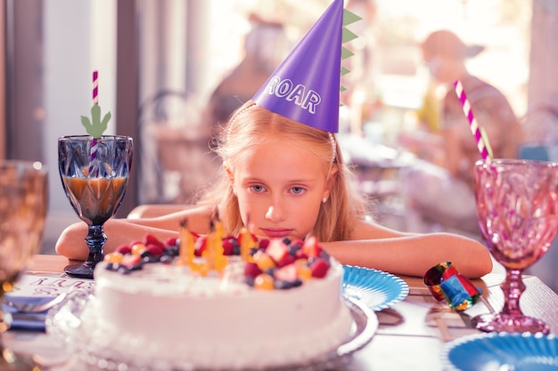 Tired girl sitting at the table and looking at her birthday cake