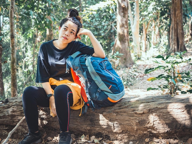 Photo tired hiking woman resting on log wood in forest with large backpack