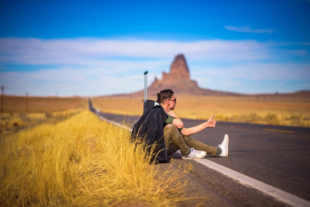 Tired hitchhiker with suitcase sitting on a road