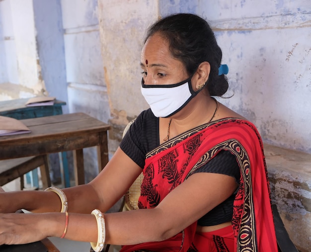 Tired Indian female teacher in face mask using a laptop computer at school during Covid-19 pandemic