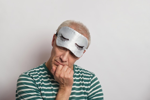 Tired man in a sleep mask on a gray background insomnia of the elderly concept sleep problems