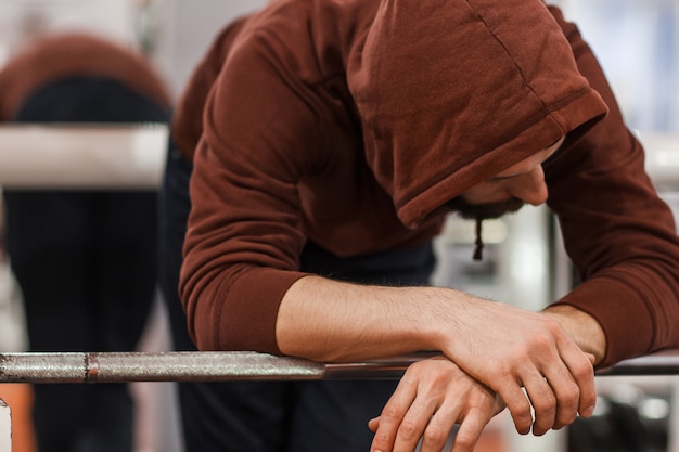 Tired man in sport hoodie leaning on barbell