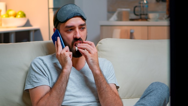 Tired man with sleep mask put talking on smartphone