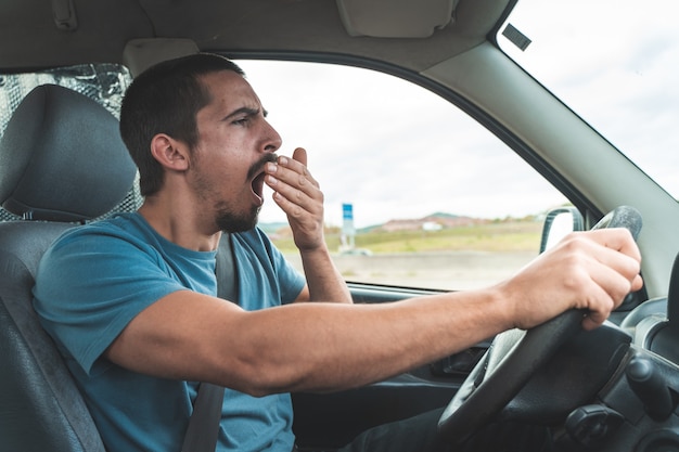 Tired man yawning while driving a car