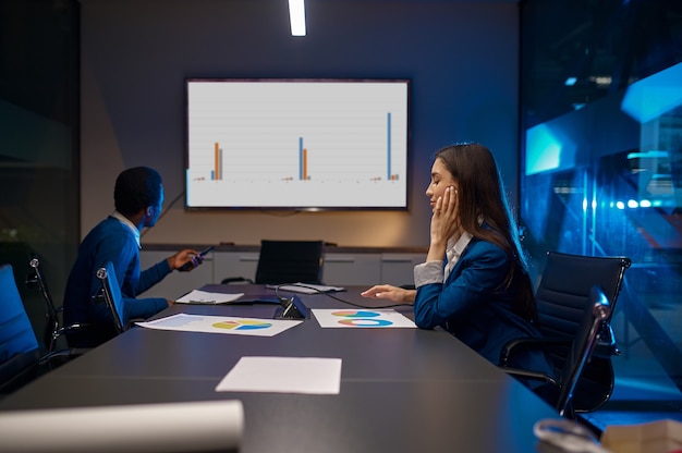 Tired manager, business presentation in night office. Male and female workers, dark business center interior, modern workplace