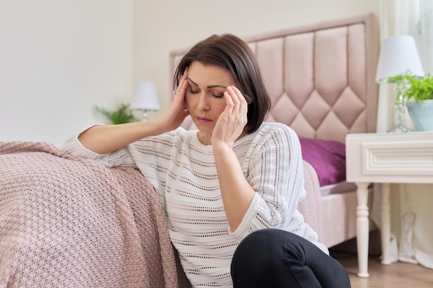 Tired mature woman suffering from headache migraine female sitting at home on the floor