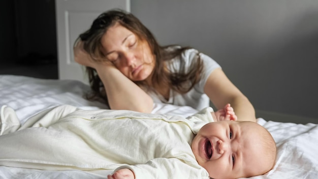 Tired mother sleeps sitting on floor near crying baby girl