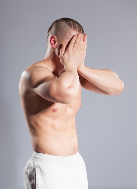 Tired muscular sportsman bodybuilder covers his face with hands